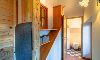 An inviting hallway with wooden details and a staircase. To the right is a bathroom with modern tiles and bright lighting.