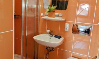 A modern bathroom with orange tiles. It has a shower, a sink, and a toilet.