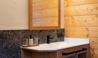A modern bathroom with a wooden washbasin and a large mirror. Skincare products and freshly folded towels are on the table.