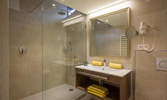A modern bathroom with a glass shower and an elegant sink. Yellow towels add a fresh accent to the space.