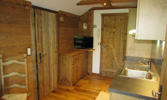 A cozy wood apartment with a small kitchen and a TV. The walls and furniture are made of light wood, creating a warm atmosphere.