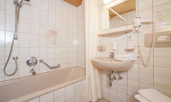 A clean bathroom with a bathtub and a sink.  
Walls and floors are tiled, and there is bright lighting.