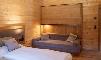 A cozy bedroom with wooden paneling. It features a bed and a sofa bed.