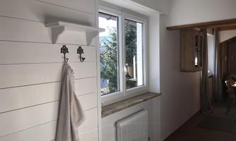 A bright room with a window and a towel rack on the wall. A few plants are on the windowsill and the floor is decorated with a carpet.