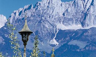 An impressive mountain landscape with high, snow-capped peaks. In the foreground stands a beautiful, historic tower.