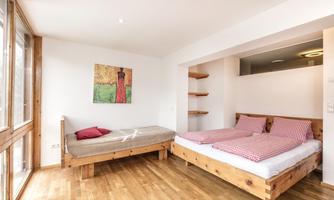 A bright bedroom with wooden flooring. There is a large bed and a single bed, as well as a painting on the wall.