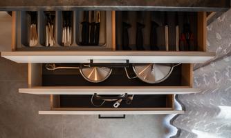 A well-organized kitchen drawer with cutlery, knives, and cooking utensils. The drawer is neatly and modernly designed.