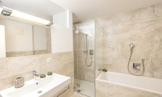 A modern bathroom with a shower and a bathtub. The walls are decorated with light tiles, and there is a simple vanity unit.