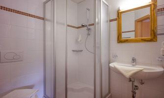 A modern bathroom with a glass shower and white tiles. In the background, there is a golden mirror and a sink.