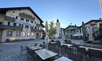 A picturesque square with beautiful buildings and a church tower in the background. Some tables and chairs are set up to enjoy the view.