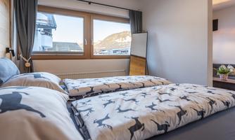 A cozy bedroom with two single beds and modern furnishings. Large windows offer a view of the mountains.