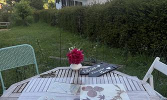 A beautiful table outdoors with pressed leaves and a flower vase. In the background, mountains and a green garden can be seen.