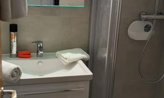 A modern bathroom with a shower and a sink. The walls are in neutral tones, and there is a large mirror light.