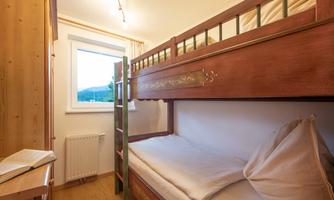 A cozy room with a bunk bed and a large window. The wooden details give the room a warm atmosphere.