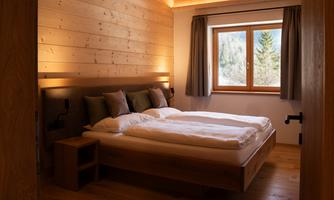 A cozy bedroom with a wooden bed and two soft pillows. Daylight streams through the window, and you can see trees in the background.