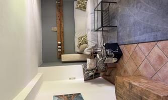A cozy living space with a white sofa and a coffee table. 

On the wall hangs a piece of art and there is a wooden shelf with decorative objects.