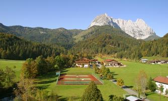 A picturesque landscape with mountains and a clear blue sky. In the foreground, there are meadows and some buildings visible.