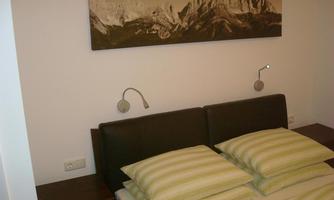 A modern bedroom with a bed and striped pillows. A picture of a mountain landscape hangs on the wall.