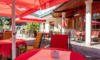 An inviting café with red umbrellas and cozy outdoor seating. The surroundings are bright and friendly, perfect for a relaxing time outdoors.