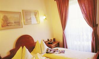 A bedroom with a comfortable bed and decorative cushions. The room has warm colors and plenty of daylight through the window.
