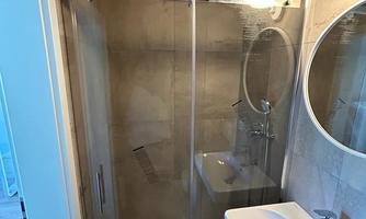 A modern shower with a glass door and rain shower. Next to the shower is a stylish sink with a mirror.