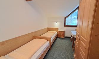 A simple room with two single beds and wooden details. A window offers a view outside.