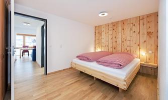 A modern bedroom with a double bed and a wooden wall panel. The room has a bright, inviting look and plenty of natural light.