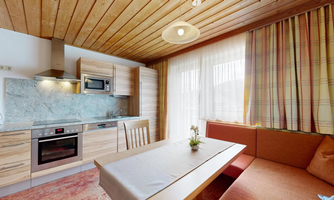 A modern kitchen with wooden details and a bright living area. The space has large windows that let in plenty of natural light.