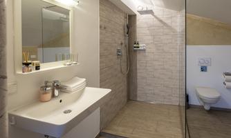 A modern bathroom with a shower, sink, and a large mirror. The walls are in light colors, and the room feels clean and inviting.