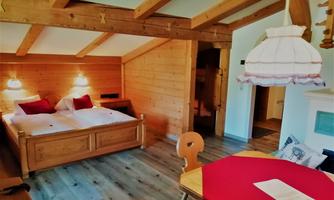 A cozy room with wood paneling and a double bed. The dining area is equipped with a table and a lamp.