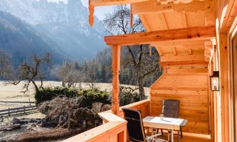 A beautiful wooden balcony overlooking a picturesque mountain landscape. The surroundings are peaceful and close to nature with a clear sky.