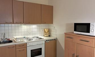 A modern kitchen with light wood cabinets and stainless steel appliances. The room features a stove, a refrigerator, and a microwave.
