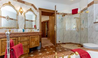 An elegant bathroom with marble tiles and luxurious fixtures. The large mirrors and golden details give the space an upscale atmosphere.