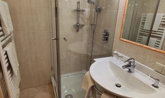 A modern bathroom with a shower and a sink. The walls are brightly tiled and there is a large mirror.