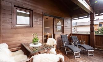 A cozy balcony with wood paneling, equipped with a table and comfortable deck chairs. Plants and cozy furs give the space an inviting atmosphere.