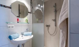 A modern bathroom with a clear glass shower and a contemporary sink. Towels and hygiene items are clearly visible.