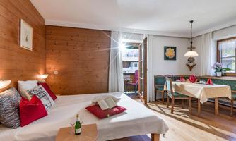 A cozy room with wooden walls and a large bed. Drinks are on the table and there is an inviting dining area.