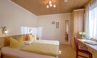 A cozy bedroom with two beds and yellow cushions. Bright wood decor and a desk next to a window create an inviting atmosphere.