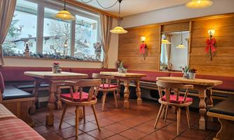 A cozy dining area with wooden tables and red chairs. Large windows offer views of a winter landscape.