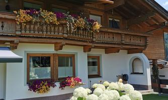 A cozy wooden house with a blooming balcony. In the foreground, there is a large bush with white hydrangeas.