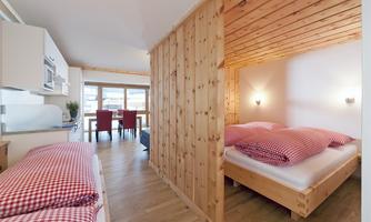 A modern room with wooden paneling and two sleeping areas. The space has a cozy atmosphere and a dining area with a table and chairs.