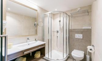 A modern bathroom with a shower, a sink, and a toilet. The walls are light and the furnishings are stylish and functional.