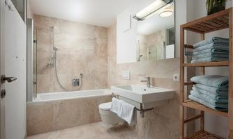 A modern bathroom with a bathtub, a shower, and a sink. On a shelf, neatly folded towels are stacked.