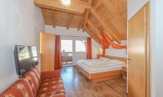 A cozy room with a wooden beam ceiling and a double bed.  
Windows with a view and a sofa complement the furnishings.