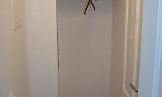 A small hallway with a wooden shelf and a clothes hanger. The walls are light and the floor is made of wood.