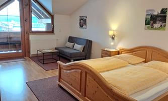 A cozy bedroom with a double bed and a seating area. The room has large windows that let in plenty of light.