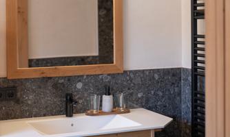 A modern bathroom with a wooden sink unit and a large mirror. Towels and toiletries are neatly arranged on the shelf.