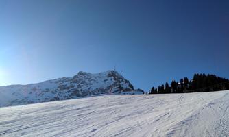 A snow-covered mountain landscape under a clear blue sky. The snow on the slope reflects the sunlight.