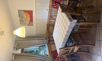 A cozy dining area with a wooden table and chairs. The windows are adorned with curtains, and a piece of art hangs on the wall.