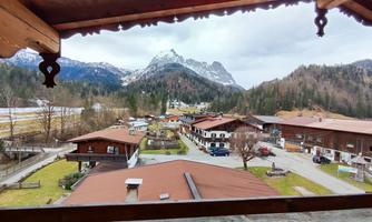A picturesque view of an alpine village with traditional wooden houses. Majestic mountains rise into the gray sky in the background.